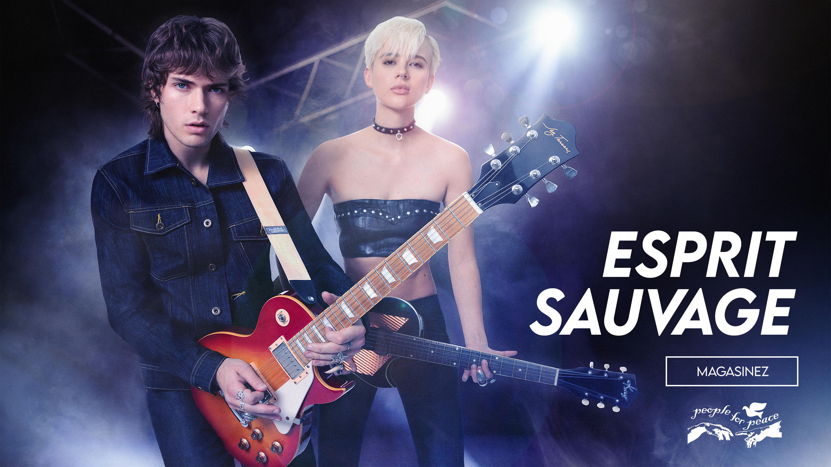 
A muscular man with short hair and tattoos stands in profile, leaning on a rustic wooden fence. He is wearing a black, sleeveless top with a white graphic print, black leather pants, and red motorcycle boots. He holds a red and black helmet in his left hand. The background is a dirt road bordered by trees, with sunlight filtering through the leaves. The image has a dark, vertical overlay on the left side with the text 'SHOW THEM GUNS THE NEW MUSCLE TEE' and 'SHOP THE 9703NS.'