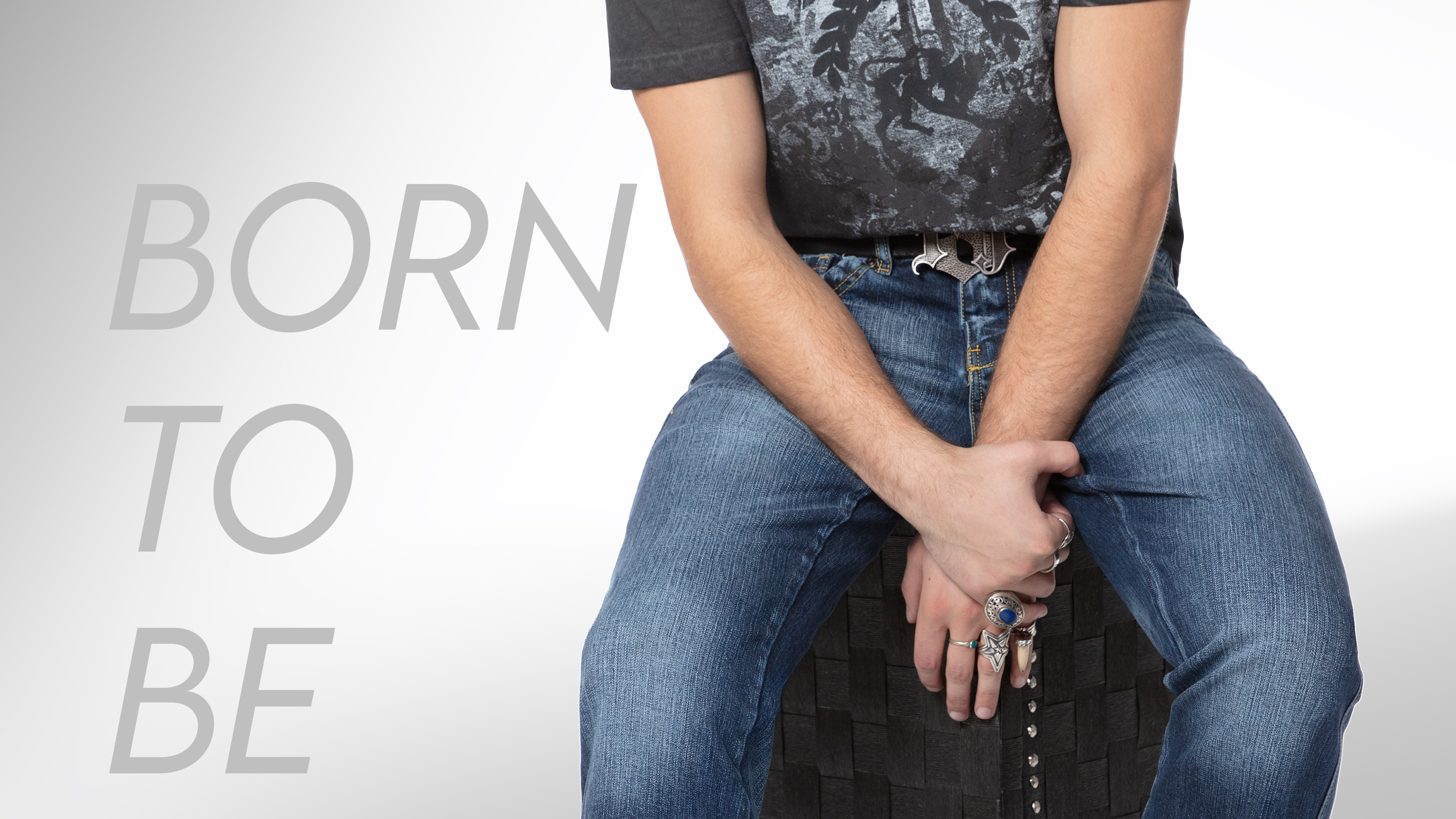 Large banner divided into three sections, 2/3. A low-angle, cropped shot of a person wearing ripped, distressed blue jeans with decorative stitching. Their hands are on their hips, and they're holding a pair of black sunglasses. The person is standing behind a black pickup truck with a red and white helmet and a red and black motocross boot resting on the tailgate. Overlaid text reads 